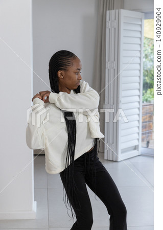 African American woman standing adjusting sleeve in white pullover and black pants near shutters African American woman standing adjusting sleeve in white pullover and black pants near shutters 140929904