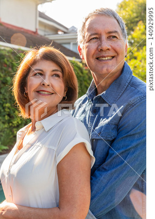 Senior couple embracing in suburban backyard, smiling while wearing white blouse and denim shirt Senior couple embracing in suburban backyard, smiling while wearing white blouse and denim shirt 140929995