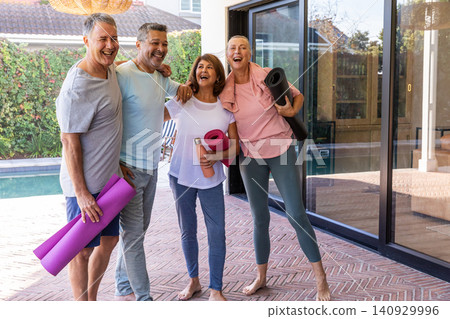 Friends standing on herringbone patio by pool in activewear holding yoga mats and water bottle Friends standing on herringbone patio by pool in activewear holding yoga mats and water bottle 140929996