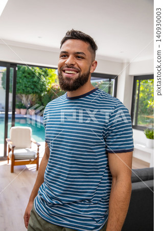Adult man standing smiling, wearing striped T-shirt and olive trousers in modern home by pool Adult man standing smiling, wearing striped T-shirt and olive trousers in modern home by pool 140930003