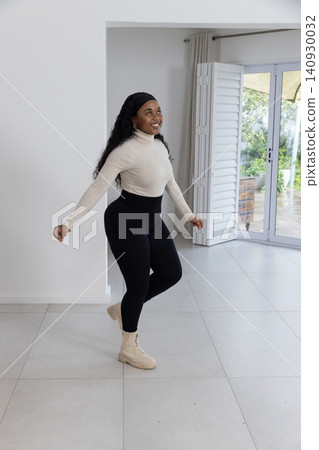 African American woman smiling, balancing foot in home wearing beige boots near sliding doors African American woman smiling, balancing foot in home wearing beige boots near sliding doors 140930032