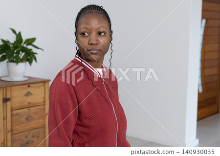 African American woman standing, wearing red zip jacket near wooden chest and potted plant at home African American woman standing, wearing red zip jacket near wooden chest and potted plant at home 140930035