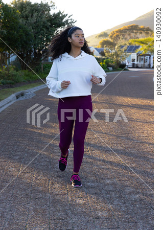 African American woman jogging on quiet street at dusk in hoodie leggings pink-laced shoes headband African American woman jogging on quiet street at dusk in hoodie leggings pink-laced shoes headband 140930092