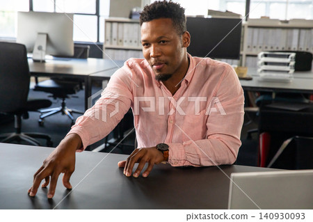African American man leaning, extending left arm across dark desk wearing watch by laptop at office African American man leaning, extending left arm across dark desk wearing watch by laptop at office 140930093