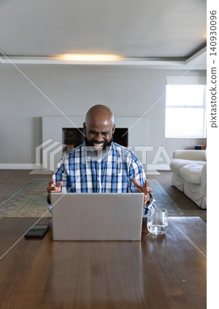Senior African American man laughing, gesturing, using laptop at home with smartphone, water glass Senior African American man laughing, gesturing, using laptop at home with smartphone, water glass 140930096