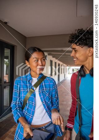 Diverse student friends walking and talking in campus corridor with tablet backpacks headphones Diverse student friends walking and talking in campus corridor with tablet backpacks headphones 140930248