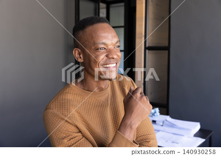 African american man wearing sweatshirt at desk smiling, looking sideways in office with papers African american man wearing sweatshirt at desk smiling, looking sideways in office with papers 140930258