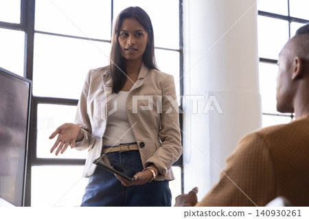 Diverse coworkers observing while presenter gesturing at tablet and monitor in office Diverse coworkers observing while presenter gesturing at tablet and monitor in office 140930261