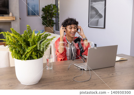 Man lifting over-ear headphones while arranging microphone and laptop on dining table Man lifting over-ear headphones while arranging microphone and laptop on dining table 140930300