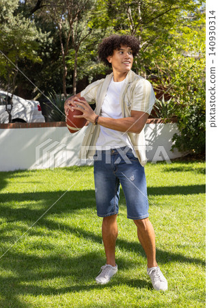African american man holding american football with both hands on lawn in residential yard African american man holding american football with both hands on lawn in residential yard 140930314