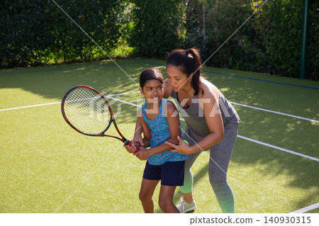 Asian mother and daughter wearing sportswear on private court and guiding grip on racket Asian mother and daughter wearing sportswear on private court and guiding grip on racket 140930315