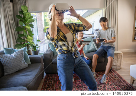 Asian friends adjusting vr headset while holding tablet and smartphone on sofa in living room Asian friends adjusting vr headset while holding tablet and smartphone on sofa in living room 140930375