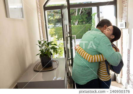 Asian father with daughter hugging at entryway wearing backpack by open door showing potted plant Asian father with daughter hugging at entryway wearing backpack by open door showing potted plant 140930376