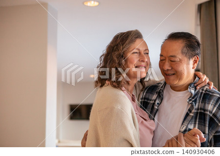 Couple embracing, swaying gently in living room with ceiling light, wall-mounted tv and curtains Couple embracing, swaying gently in living room with ceiling light, wall-mounted tv and curtains 140930406