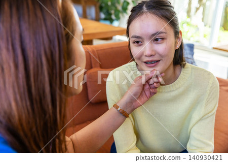 Asian mother comforting teenage daughter on couch by window with houseplant Asian mother comforting teenage daughter on couch by window with houseplant 140930421