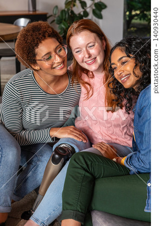 Diverse female friends leaning in smiling on couch at home with prosthetic leg Diverse female friends leaning in smiling on couch at home with prosthetic leg 140930440