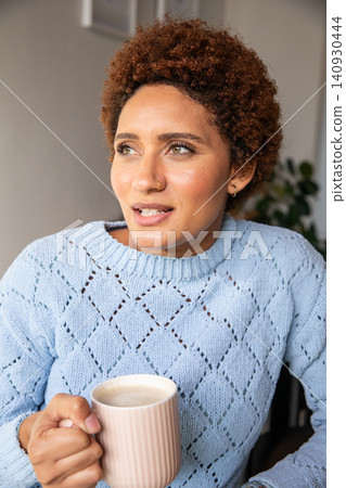 African american woman holding ribbed mug at home, gazing left at framed artwork, plant African american woman holding ribbed mug at home, gazing left at framed artwork, plant 140930444