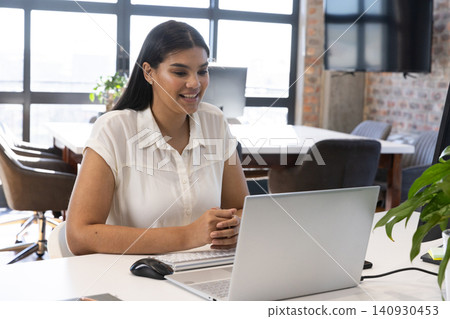 Asian woman wearing collared blouse typing on wireless keyboard at office desk with laptop Asian woman wearing collared blouse typing on wireless keyboard at office desk with laptop 140930453