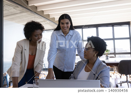 Diverse female coworkers collaborating near laptop on meeting table in conference room Diverse female coworkers collaborating near laptop on meeting table in conference room 140930456