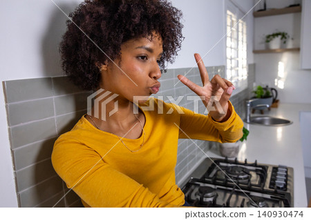African american woman leaning against backsplash in kitchen near gas cooktop with peace sign African american woman leaning against backsplash in kitchen near gas cooktop with peace sign 140930474
