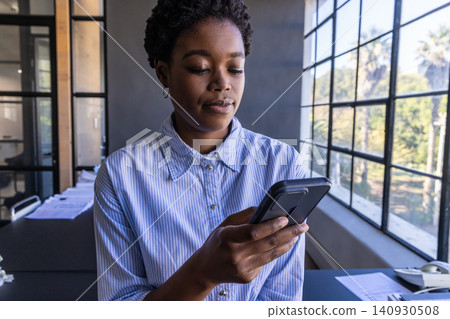African american woman holding smartphone and reviewing documents at office desk African american woman holding smartphone and reviewing documents at office desk 140930508