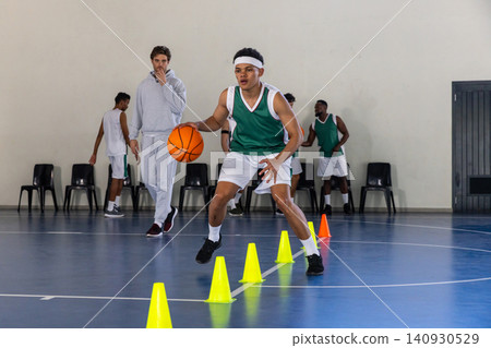 African american male basketball player dribbling basketball through yellow cones on court African american male basketball player dribbling basketball through yellow cones on court 140930529