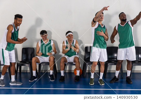 Diverse male teammates in green uniforms celebrating and clapping on gym with basketball Diverse male teammates in green uniforms celebrating and clapping on gym with basketball 140930530