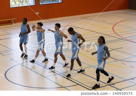 Diverse male teammates walking diagonally across gym colored court lines wearing matching jerseys Diverse male teammates walking diagonally across gym colored court lines wearing matching jerseys 140930555
