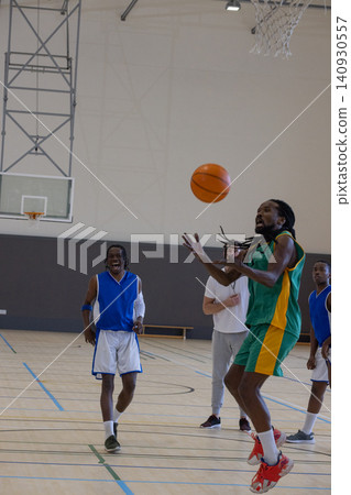 Diverse male players in jerseys jumping and reaching for basketball on court under hoop Diverse male players in jerseys jumping and reaching for basketball on court under hoop 140930557