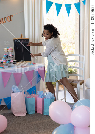 Pregnant african american woman arranging pink, blue cupcakes next to chalkboard in living room Pregnant african american woman arranging pink, blue cupcakes next to chalkboard in living room 140930635