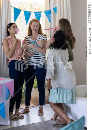 Diverse female friends celebrating baby shower in living room holding pacifier props, infant Diverse female friends celebrating baby shower in living room holding pacifier props, infant 140930638