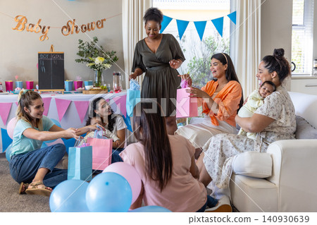 Diverse women friends opening gifts with baby and toddler under baby shower banner 140930639