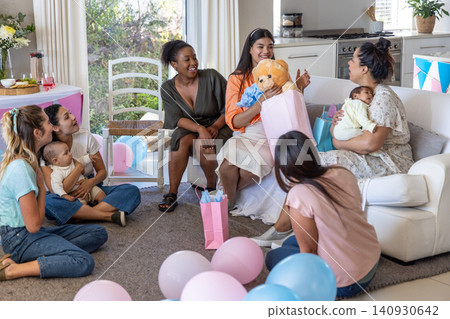 Diverse female friends celebrating baby shower at home with pink-blue balloons gift, bags Diverse female friends celebrating baby shower at home with pink-blue balloons gift, bags 140930642
