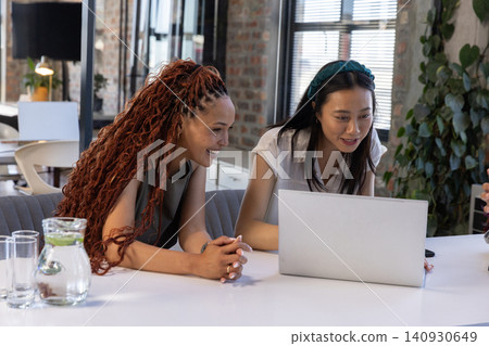 Diverse female coworkers collaborating on silver laptop near glass water pitcher at office 140930649