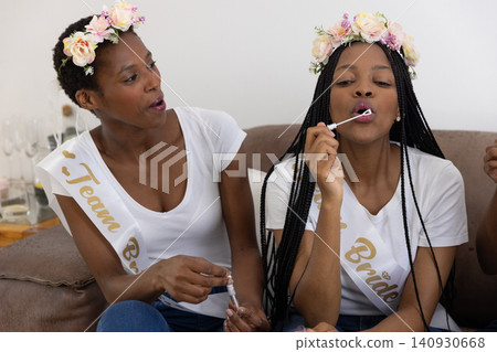 African American women sitting on couch at home with bride sashes blowing bubbles with bubble wand African American women sitting on couch at home with bride sashes blowing bubbles with bubble wand 140930668