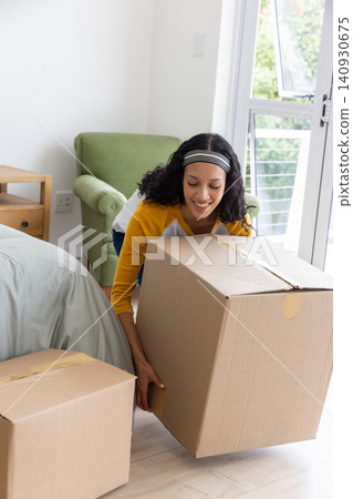 Teenage girl crouching and lifting one of two sealed cardboard boxes in bedroom Teenage girl crouching and lifting one of two sealed cardboard boxes in bedroom 140930675