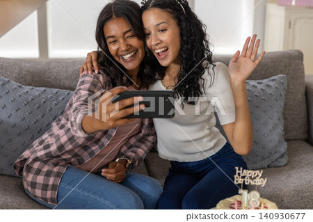 Diverse mom and teenage daughter taking selfie on sofa at home with smartphone and birthday cake Diverse mom and teenage daughter taking selfie on sofa at home with smartphone and birthday cake 140930677