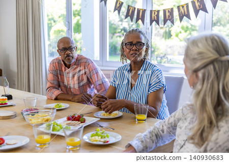 Diverse senior friends gathering at table sharing fruit and juice, celebrating retirement Diverse senior friends gathering at table sharing fruit and juice, celebrating retirement 140930683