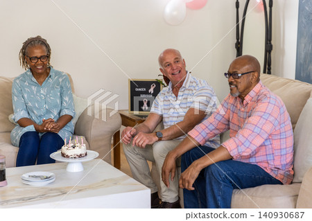Diverse senior friends celebrating milestone in home living room with cake, survivor sign Diverse senior friends celebrating milestone in home living room with cake, survivor sign 140930687