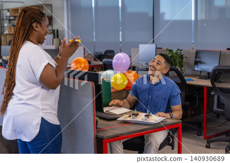 Diverse coworkers celebrating and clapping at modern office workstation with lit cupcakes Diverse coworkers celebrating and clapping at modern office workstation with lit cupcakes 140930689
