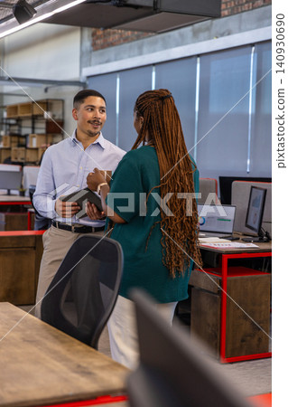 Diverse coworkers in business attire talking, holding tablet, coffee mug at office near monitors Diverse coworkers in business attire talking, holding tablet, coffee mug at office near monitors 140930690