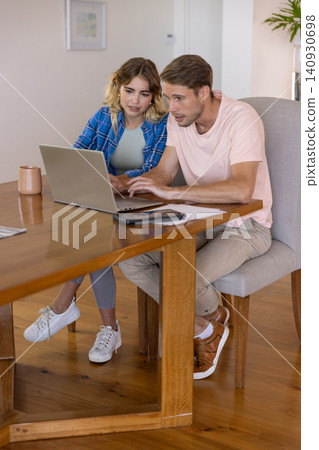 Couple working on laptop at dining table at home with coffee mug, papers and smartphone Couple working on laptop at dining table at home with coffee mug, papers and smartphone 140930698