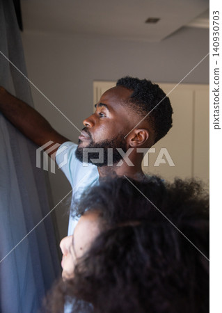 African american couple standing by window pulling back curtains at home, ceiling vent 140930703