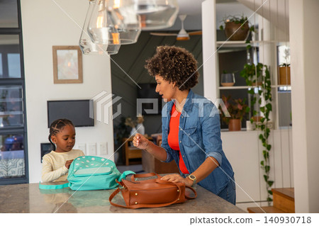 Diverse mother with daughter unpacking turquoise backpack on kitchen counter near leather handbag Diverse mother with daughter unpacking turquoise backpack on kitchen counter near leather handbag 140930718