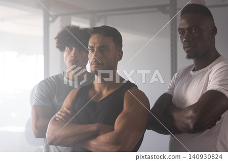 Diverse male gym partners standing shoulder to shoulder in gym by squat rack, barbell and plates Diverse male gym partners standing shoulder to shoulder in gym by squat rack, barbell and plates 140930824