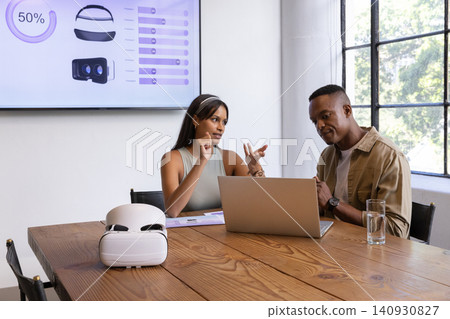 Gesturing at laptop, vr headset, diverse coworkers discussing vr hardware in meeting room Gesturing at laptop, vr headset, diverse coworkers discussing vr hardware in meeting room 140930827