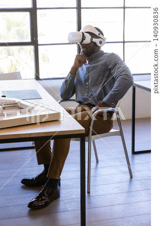 African american man wearing vr gear examining architectural model on desk at design studio African american man wearing vr gear examining architectural model on desk at design studio 140930836