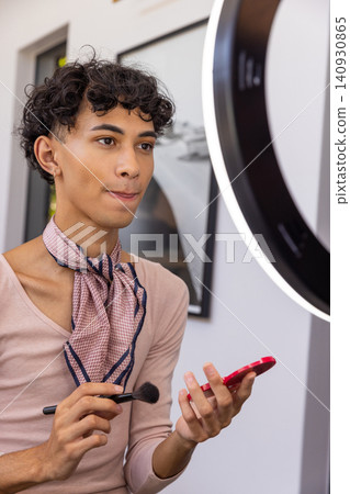 Man holding compact mirror and applying makeup in studio with ring light near framed photograph Man holding compact mirror and applying makeup in studio with ring light near framed photograph 140930865