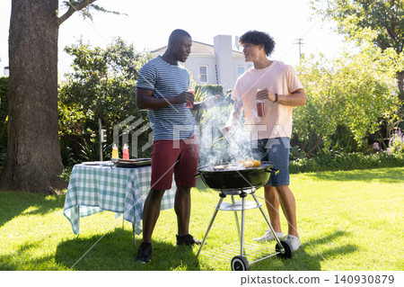 Diverse male friends barbecuing near grill and checkered table with condiments in backyard 140930879