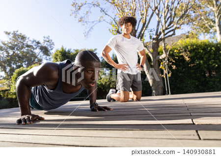 Diverse male fitness partners doing push-ups on wooden deck with partner 140930881